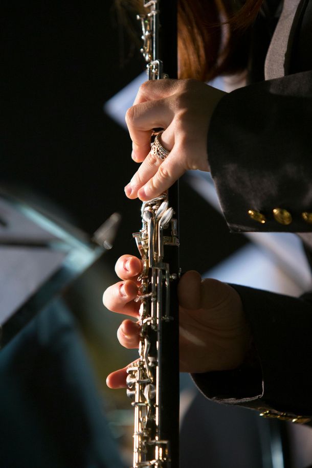 Hands playing an oboe, focusing on the keys. The musician wears a dark jacket.