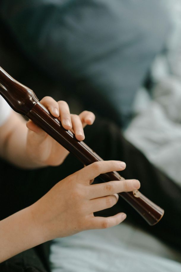 Person playing a dark brown recorder with their hands on the instrument, indoors.
