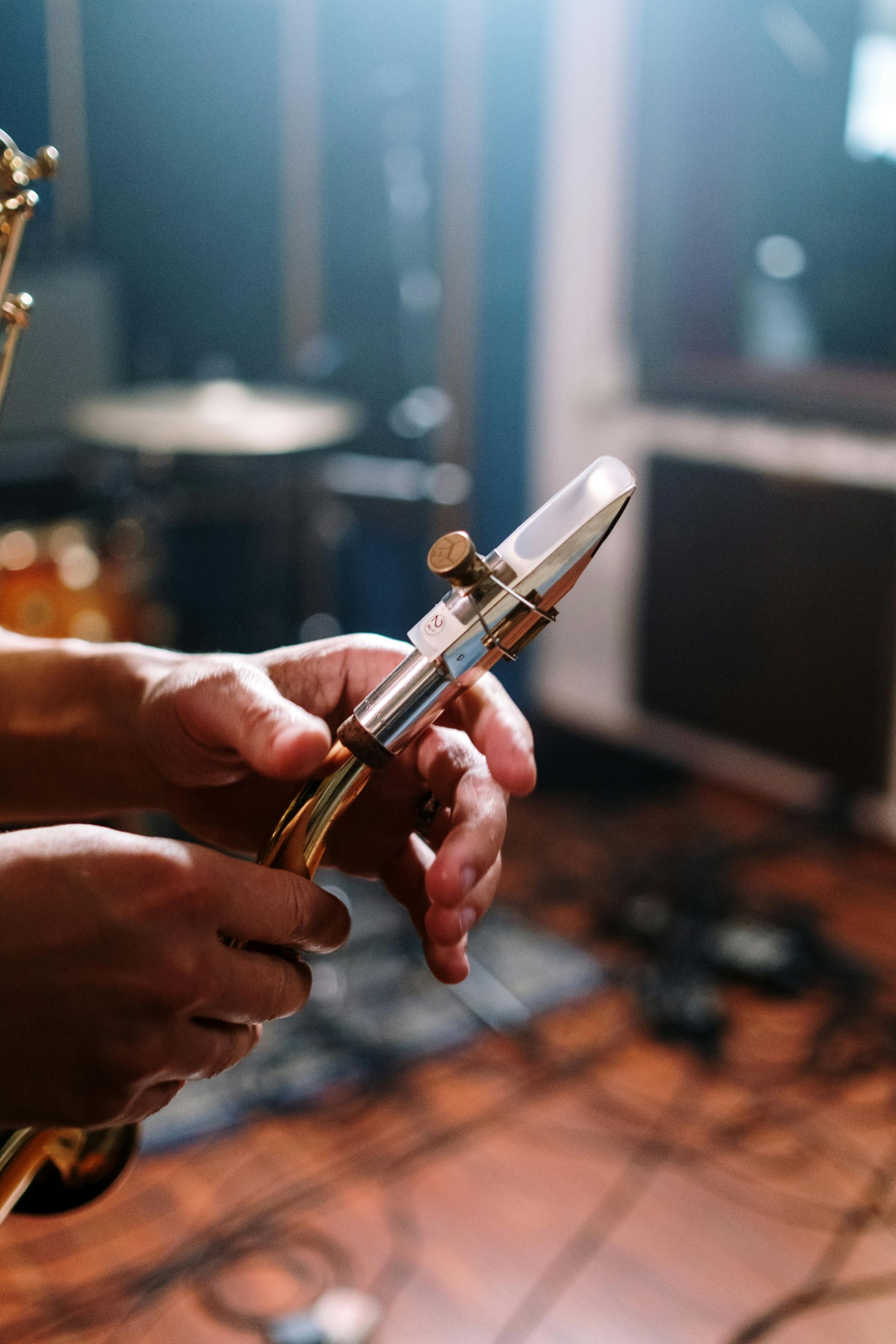 Hands holding a saxophone mouthpiece, with a recording studio background.