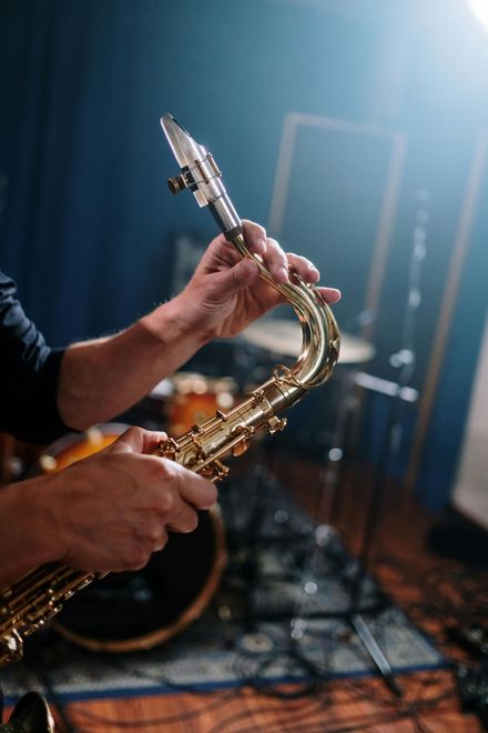 Person holding a gold saxophone, hands on the instrument. Studio setting, blue wall.