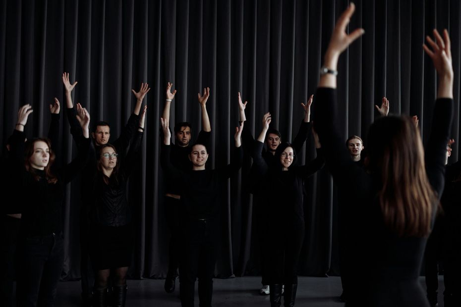 A group of people in black with raised arms, facing forward in a dark room.