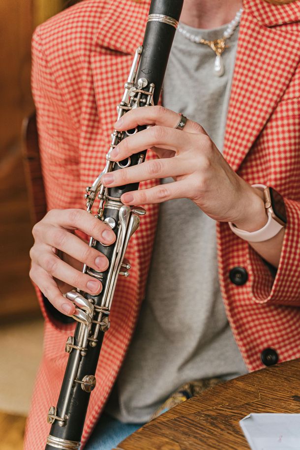 Person playing a black clarinet, wearing a pink plaid jacket and gray shirt, hands visible.