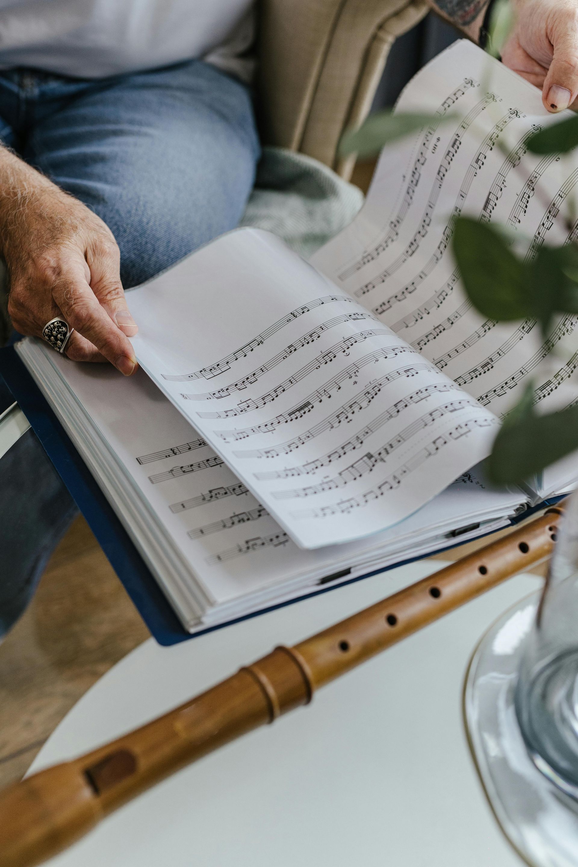 Person flipping through sheet music, with a recorder on a table.