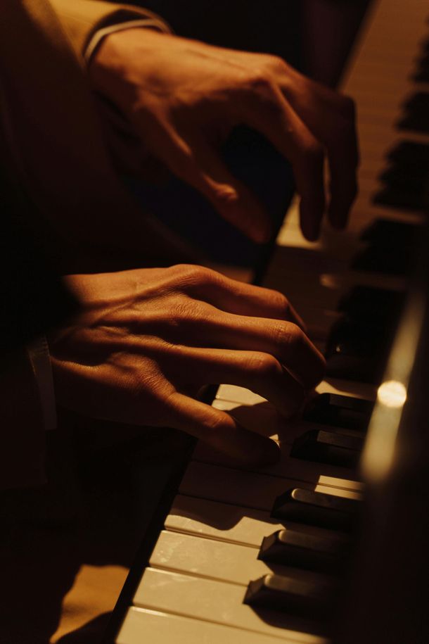 Hands playing a piano, lit by warm light.