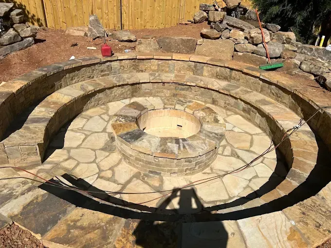 Circular stone fire pit with tiered seating under construction outdoors.