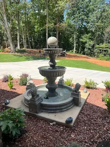 A multi-tiered outdoor water fountain with a stone base, surrounded by landscaping.