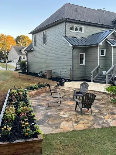 Backyard patio with stone paving, seating, and a raised garden bed against a two-story home.