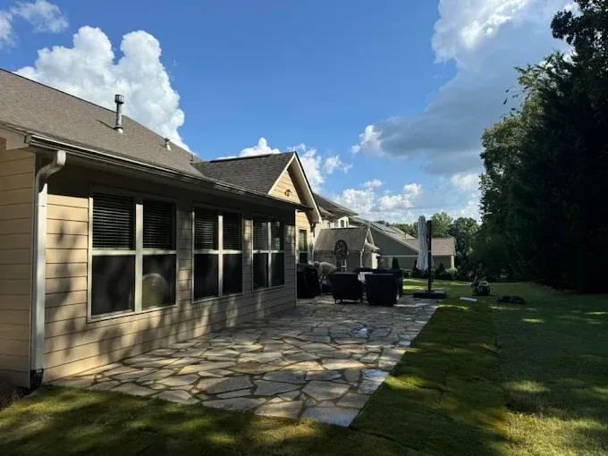 Patio with stone pavers, house with windows, blue sky, and green grass.
