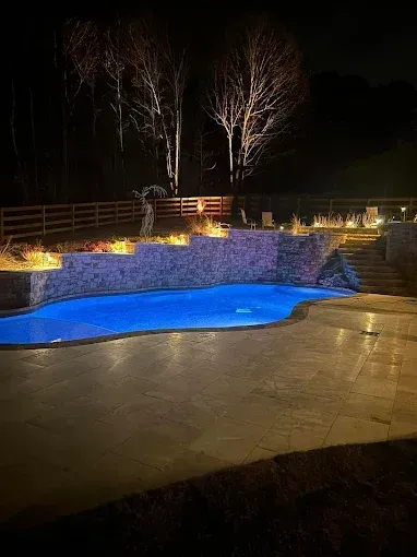 Nighttime pool scene with blue illuminated water, stone walls, and ambient lighting.