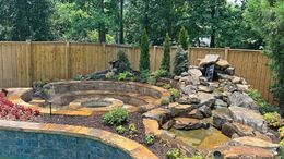 Stone waterfall feature with tiered seating, plants, and a pool.