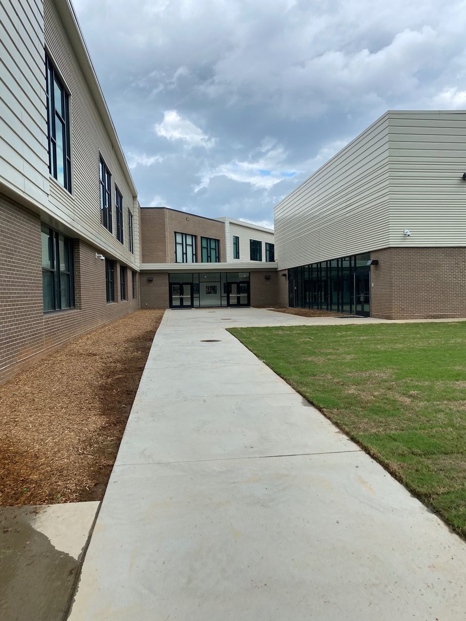 Exterior of modern school buildings, walkway leading to entry doors. Overcast sky.