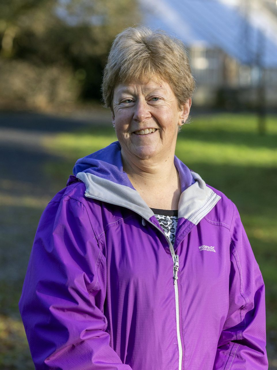 Smiling cartoon woman with wavy brown hair, wearing a purple shirt, and rosy cheeks.