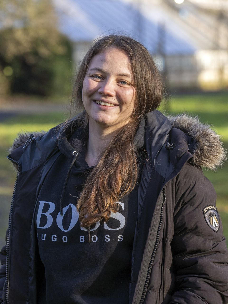Chef standing in a cafe, leaning on a counter displaying snacks. He wears glasses and a chef's coat, smiling.