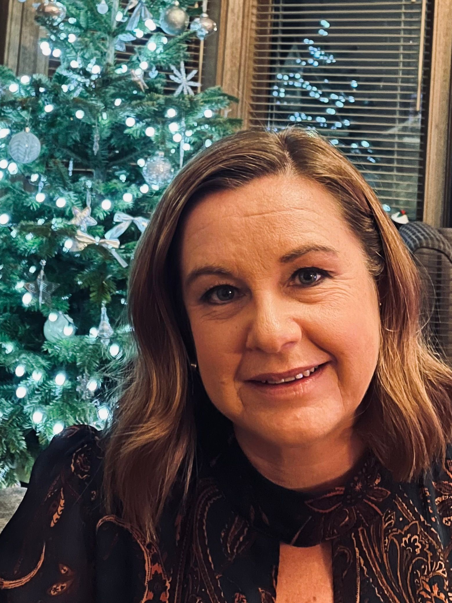 Smiling cartoon woman with wavy brown hair, wearing a purple shirt, and rosy cheeks.