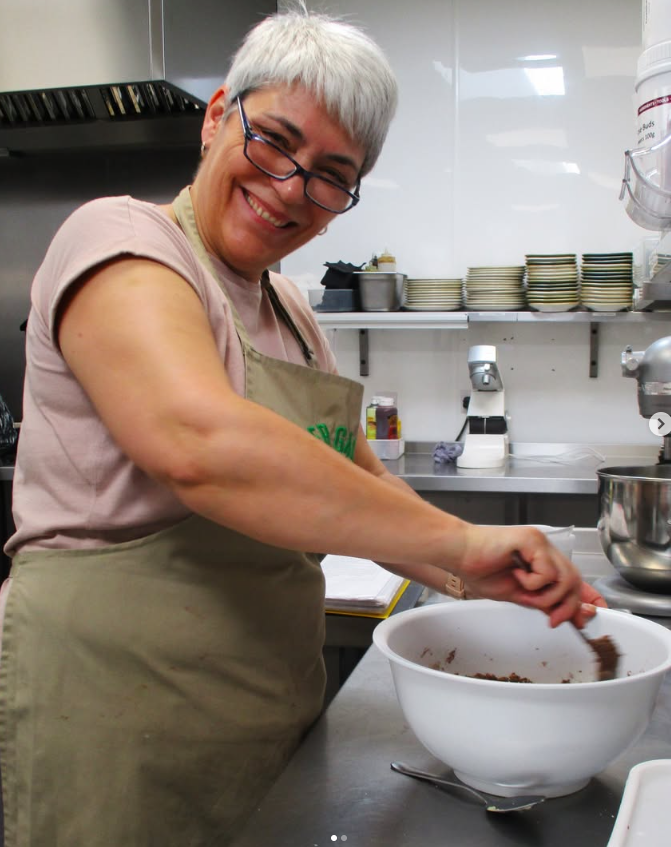 Woman mixing batter in a white bowl, smiling in a commercial kitchen.