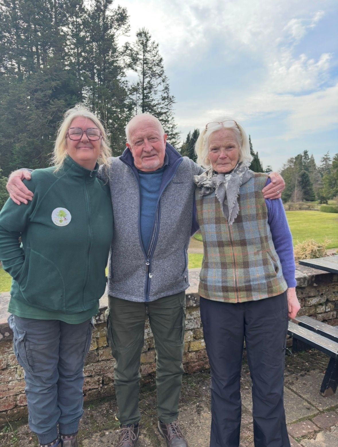 Picture of three people standing outside with their arms around each other smiling at the camera.