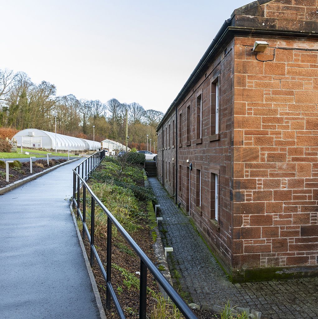 Brick building and pathway with black railing next to a row of greenhouses.