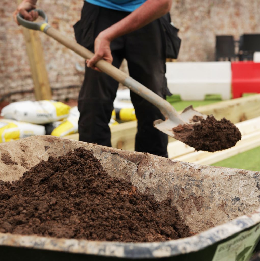 Person shoveling dirt into a wheelbarrow outdoors, construction setting.