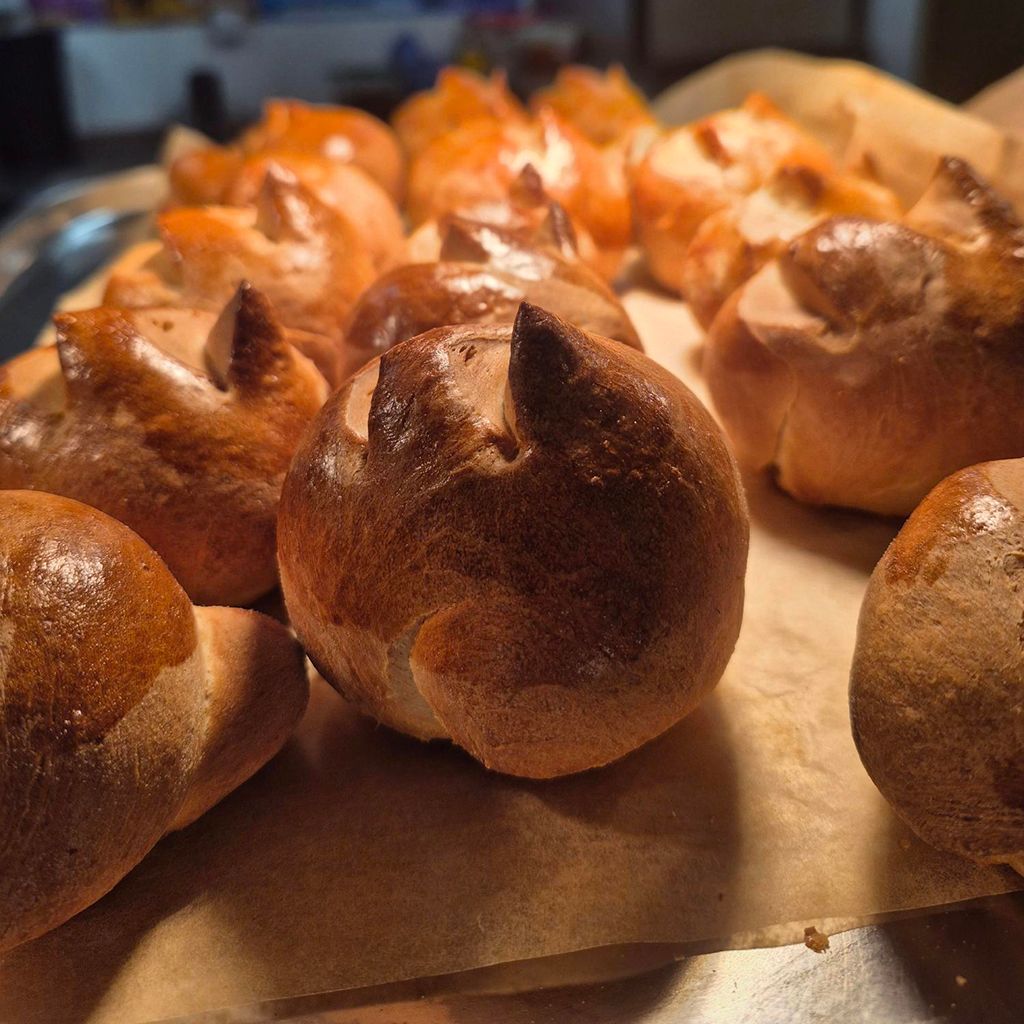 Close-up of golden-brown brioche rolls with pointed tops, on parchment paper.