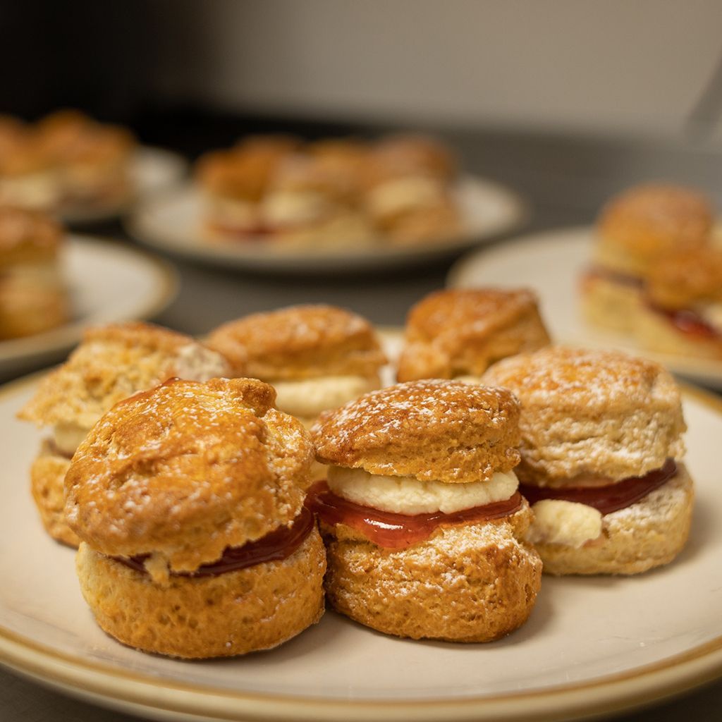 Close-up of scones, some with cream and jam, on plates.