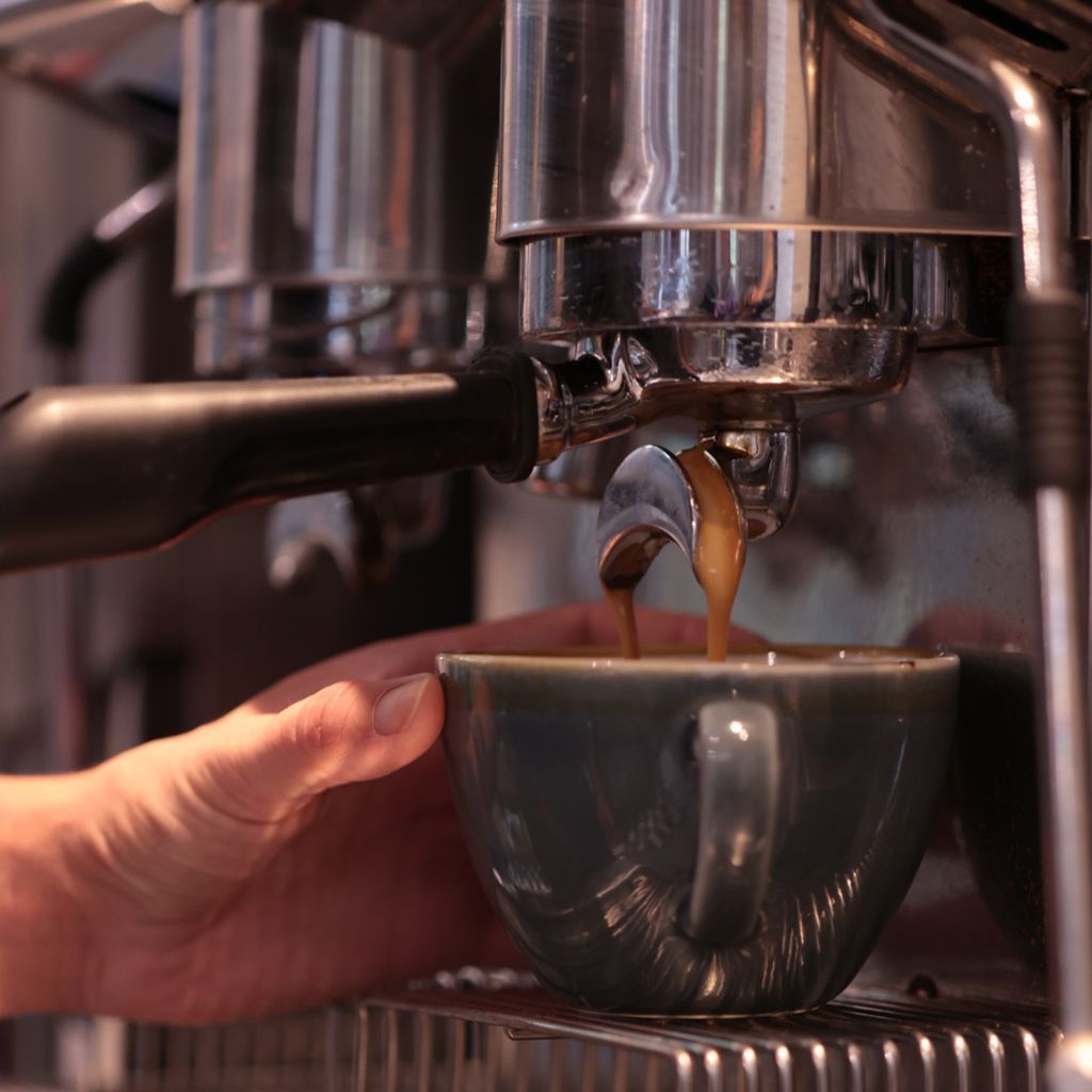 Espresso machine dispensing coffee into a dark mug, hand holding the cup.
