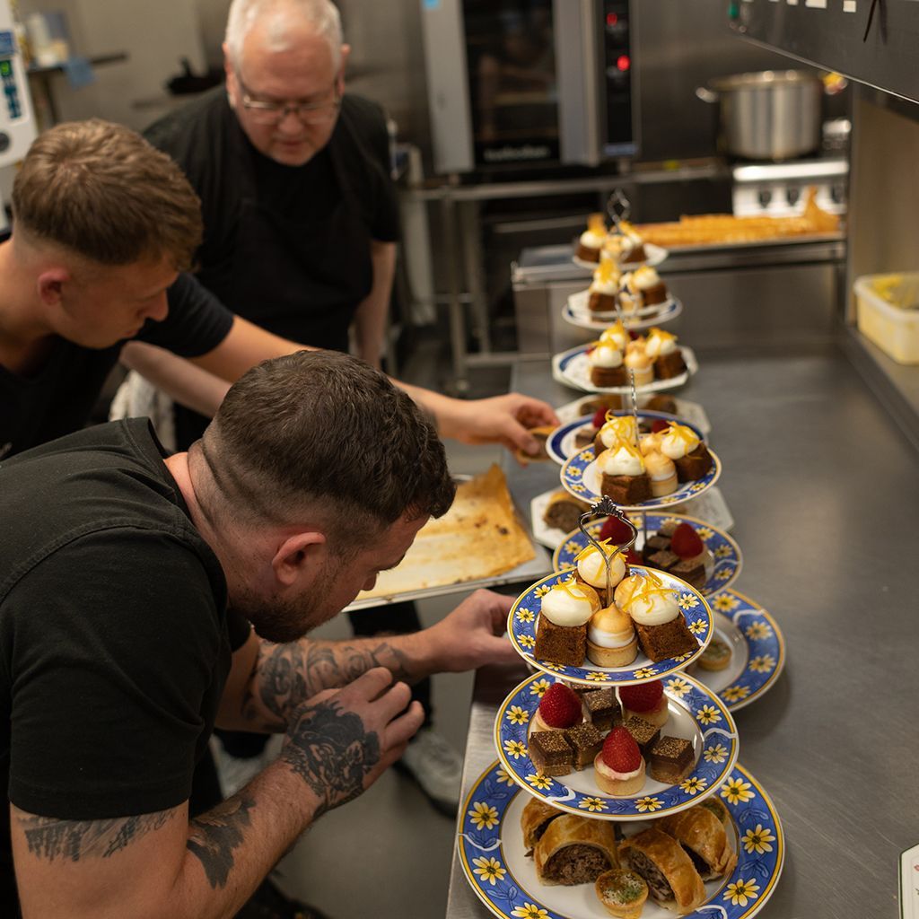 Chefs arranging desserts on tiered plates in a commercial kitchen.