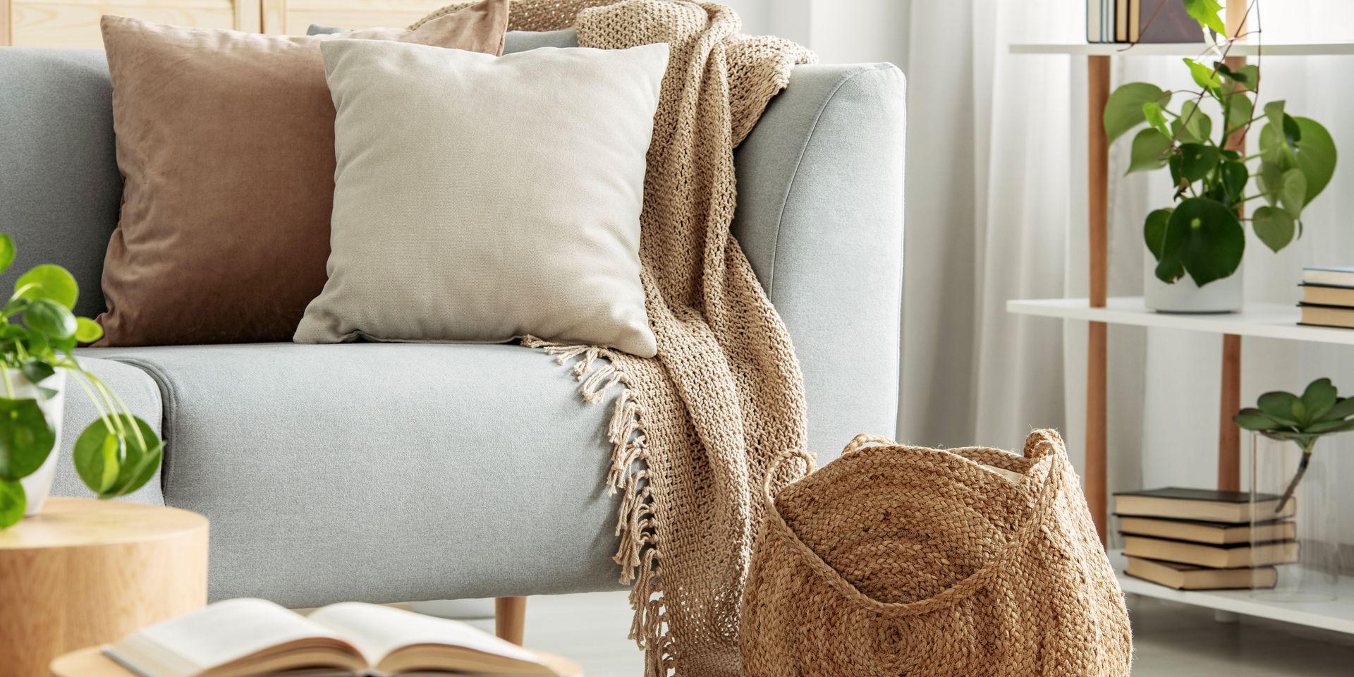 A living room scene featuring a light blue sofa with throw pillows and a knitted blanket. A woven basket sits at the sofa's base.