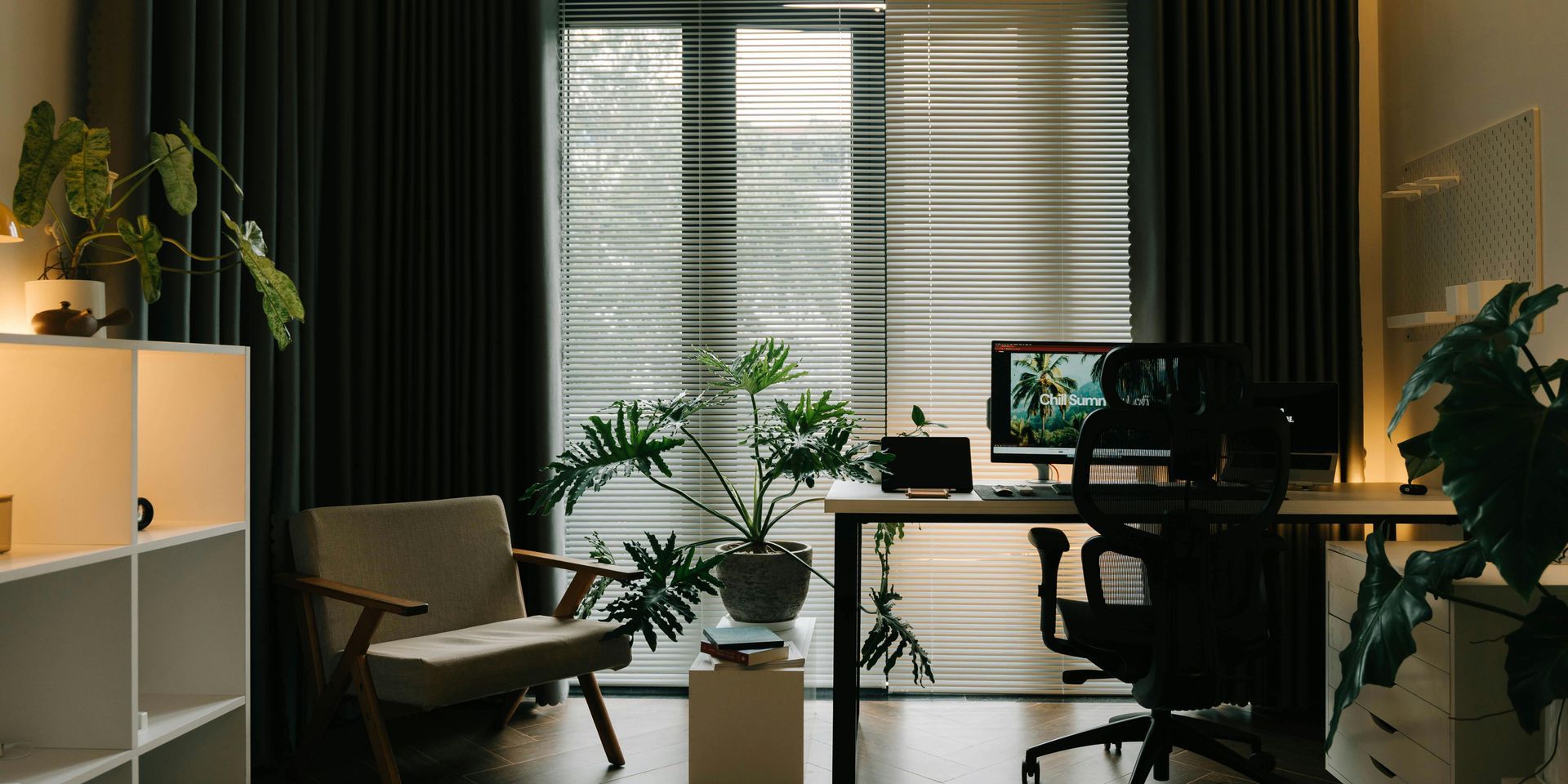 A modern home office with dark curtains, a desk with a computer, and plants.