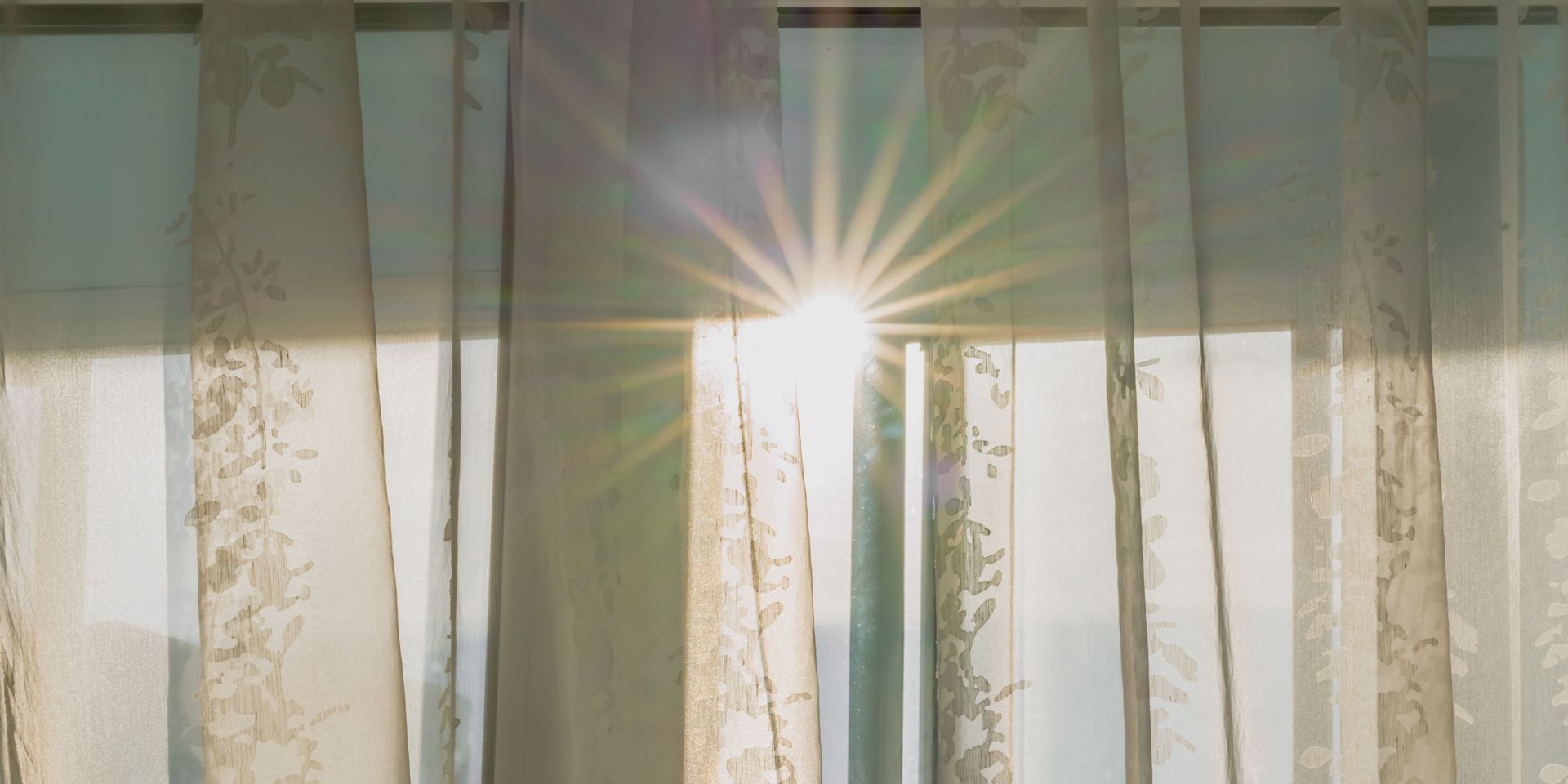 The sun is shining through the curtains of a window.
