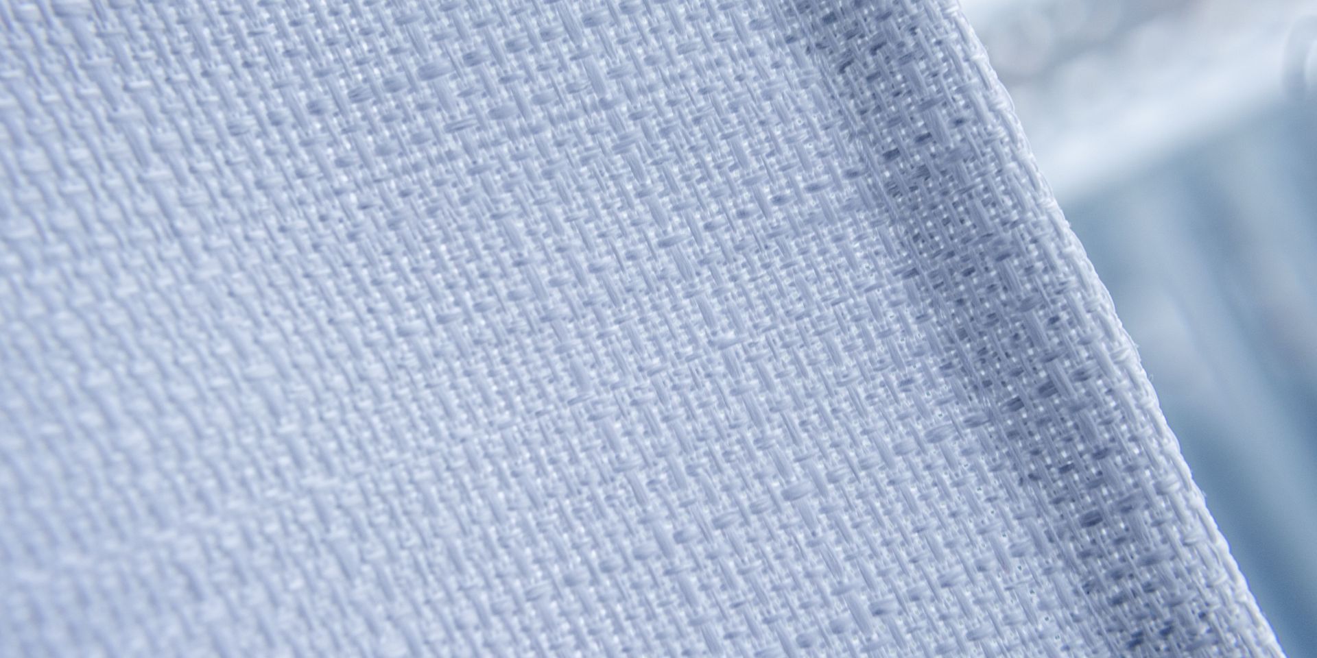Close-up of a light blue fabric with a textured weave and stitched edge.