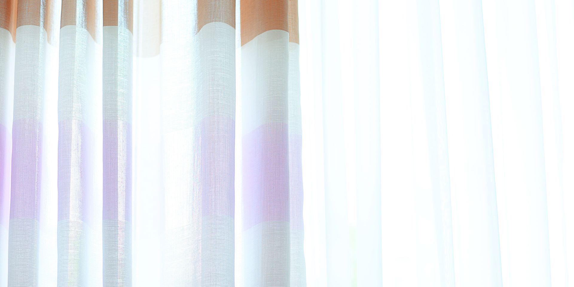 A row of white curtains hanging on a window with a white background.