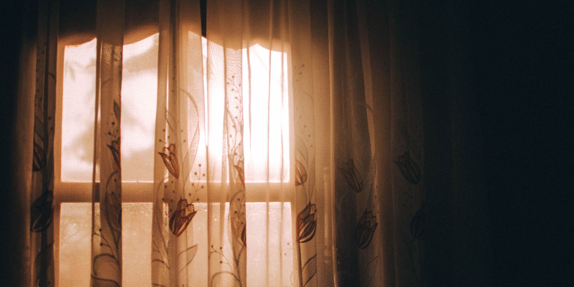 The sun is shining through the curtains of a window.