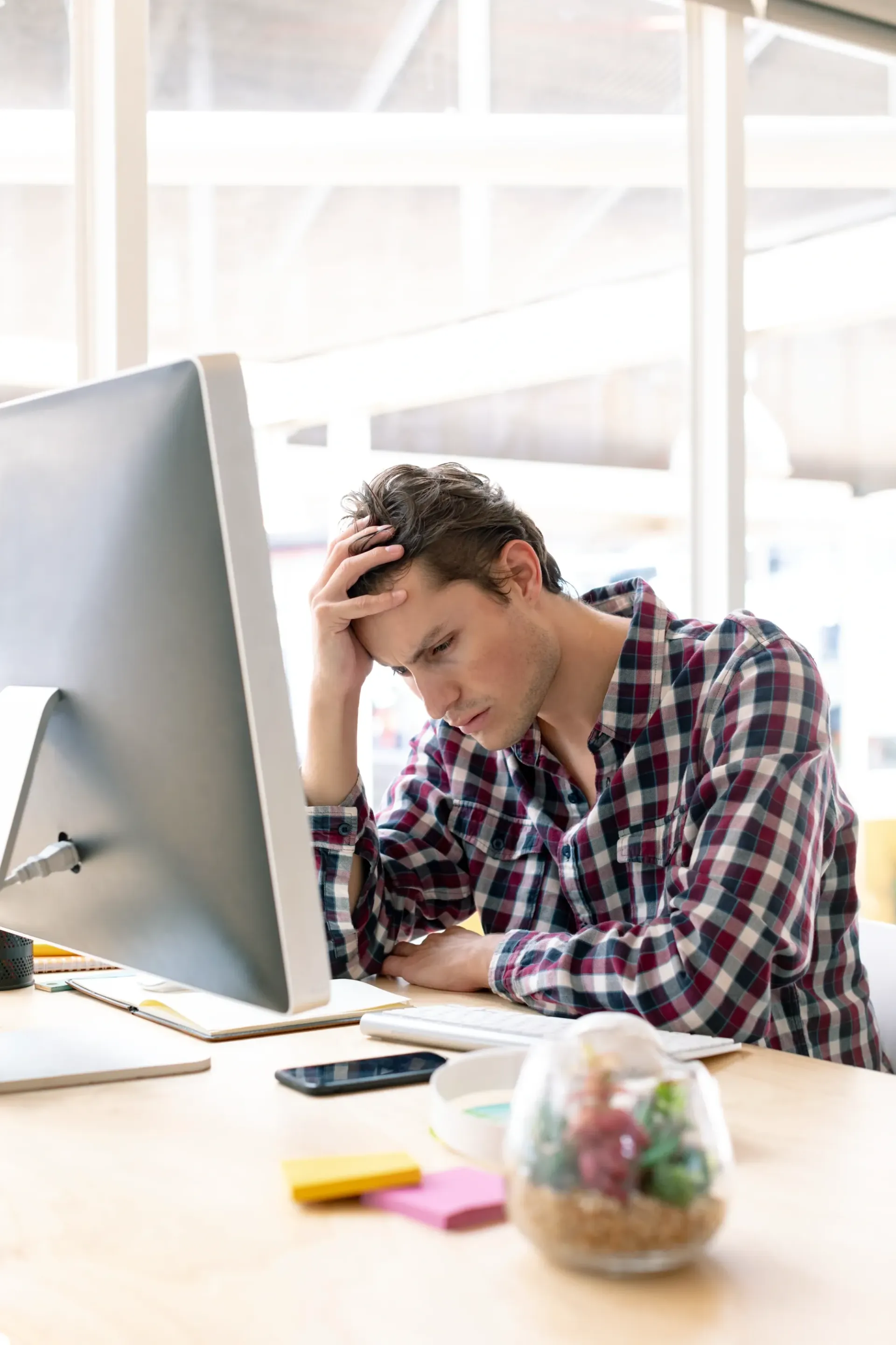 Man at desk, looking stressed, hand on head, in front of a computer, office setting.