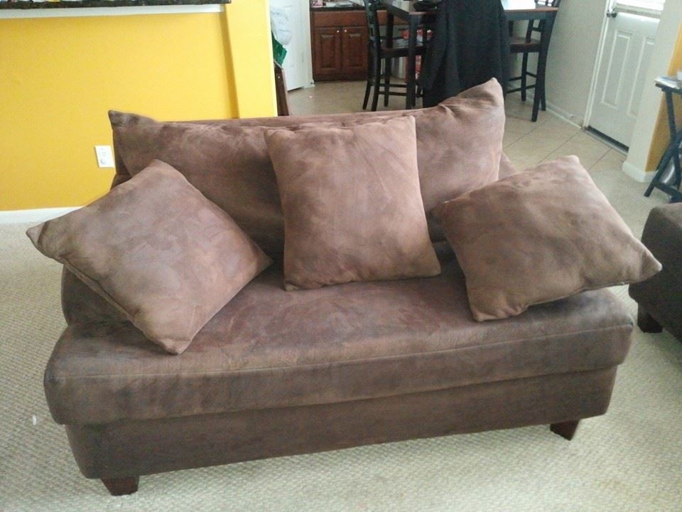 Brown loveseat with four matching pillows in a room with a yellow wall and a glimpse of a kitchen.