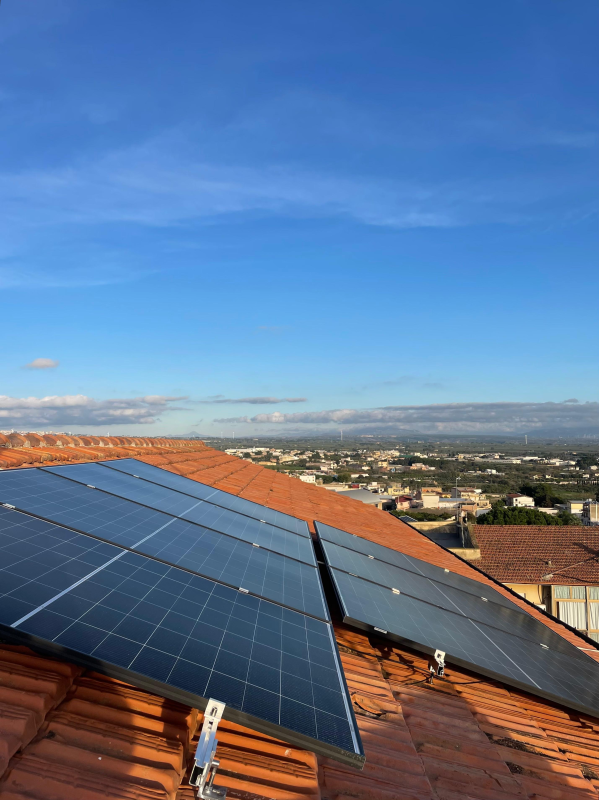 Pannelli solari su un tetto di tegole rosse con lo skyline della città sullo sfondo sotto un cielo azzurro.