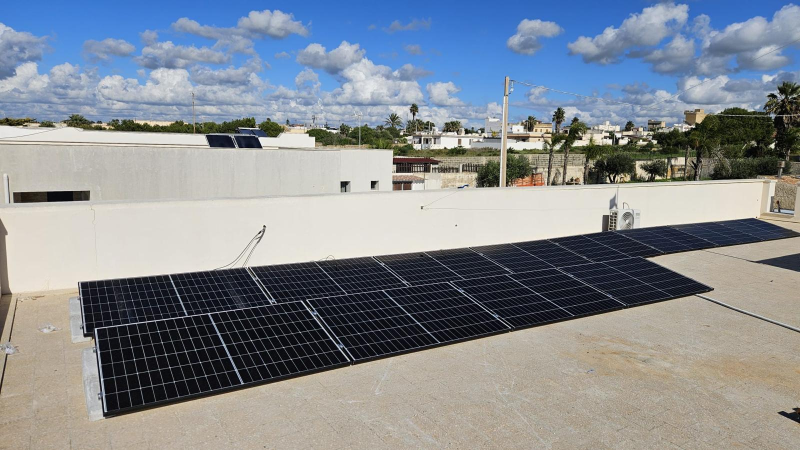 Pannelli solari su un tetto bianco sotto un cielo azzurro con nuvole soffici.