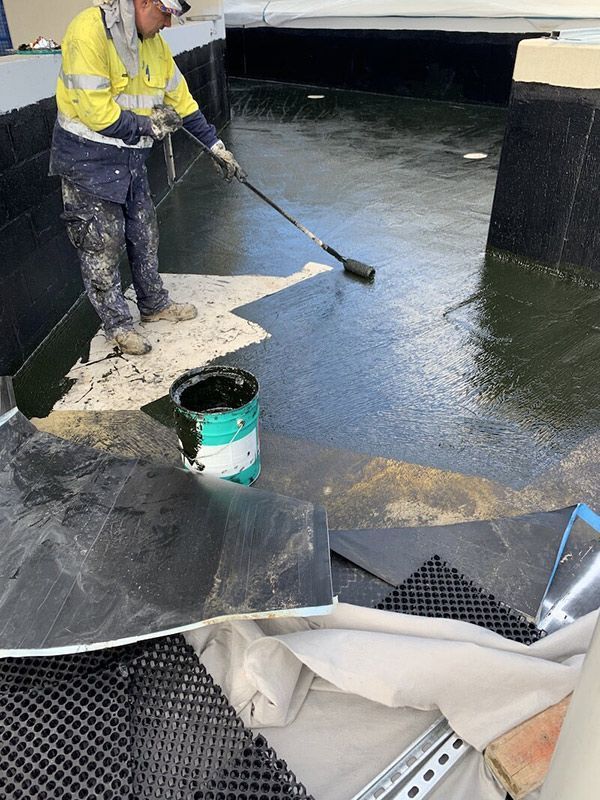 A Man Is Painting A Concrete Floor With A Roller — Eldred Waterproofing In Whitfield, QLD