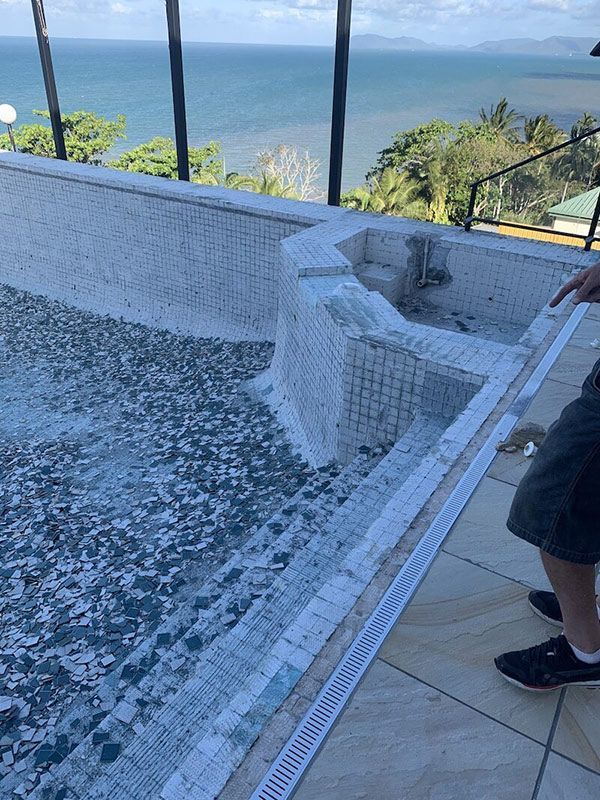 A Man Is Standing Next To A Swimming Pool With A View Of The Ocean — Eldred Waterproofing In Whitfield, QLD