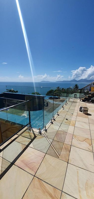 A Balcony With A Glass Railing Overlooking The Ocean — Eldred Waterproofing In Whitfield, QLD