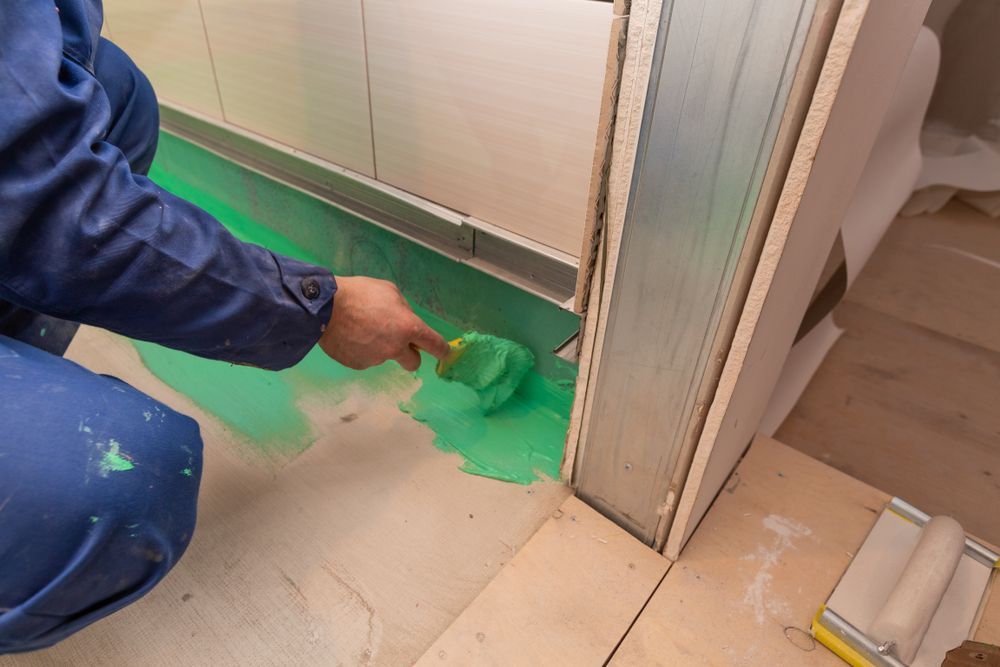 A Man Is Painting The Floor Of A Bathroom With A Brush — Eldred Waterproofing In Cairns, QLD