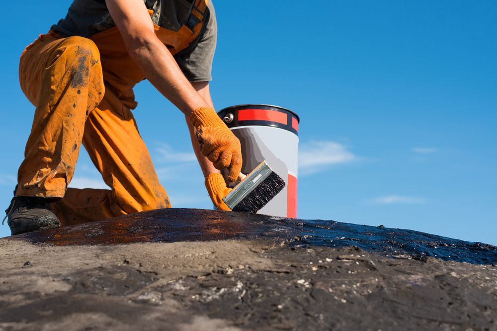 A Man Is Kneeling Down And Painting A Roof With A Brush — Eldred Waterproofing In Trinity Beach, QLD