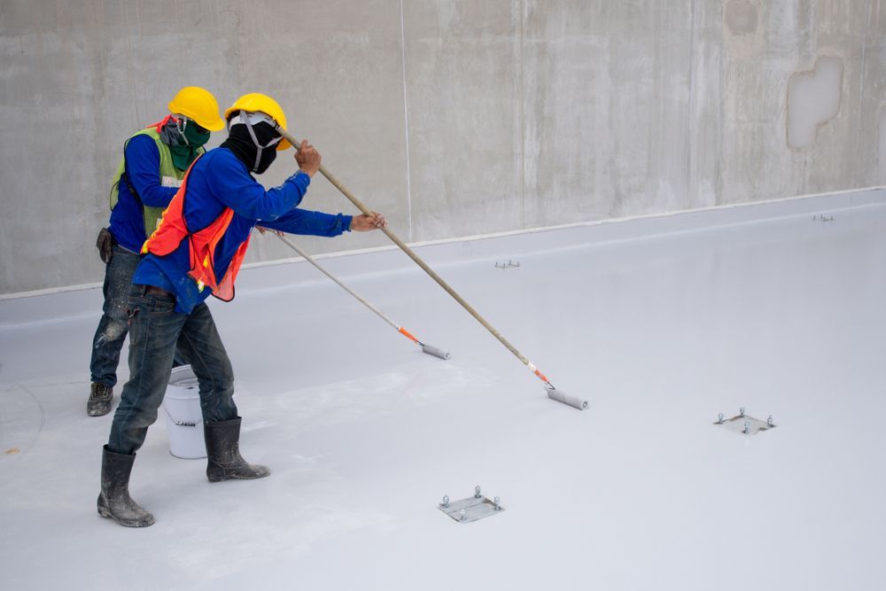 Two Construction Workers Are Painting The Floor Of A Building — Eldred Waterproofing In Whitfield, QLD