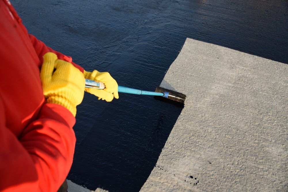 A Person Wearing Yellow Gloves Is Painting A Concrete Surface — Eldred Waterproofing In Whitfield, QLD