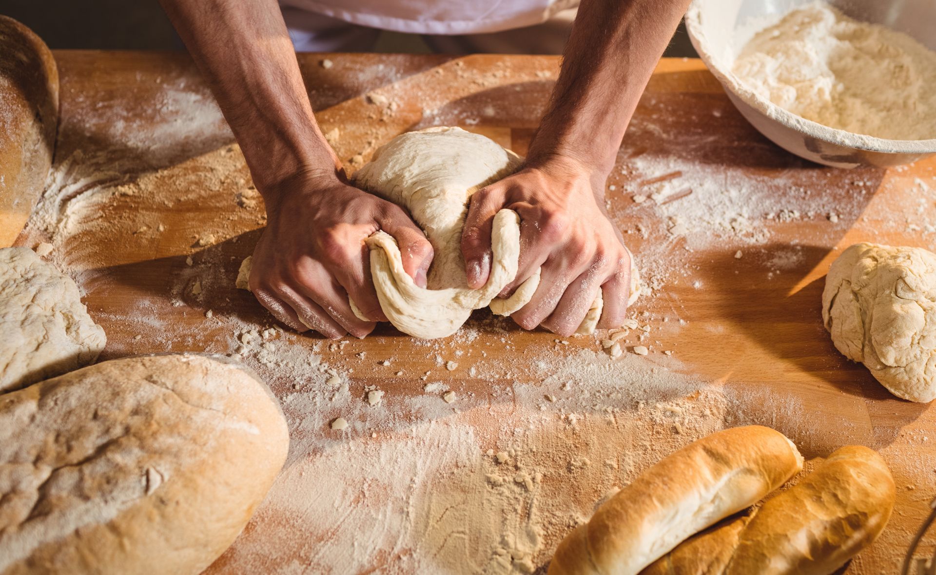 The hands of a baker knead a mound of dough to make bread.