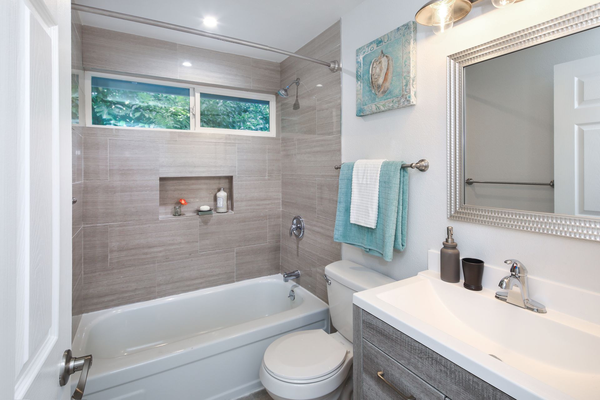 A light, neutral-toned bathroom with a tub-shower combo, wood-look tile walls, a white toilet, and a vanity with a mirror.
