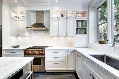 Bright, modern kitchen with white cabinetry, marble countertops, stainless steel appliances, and a window above the sink.