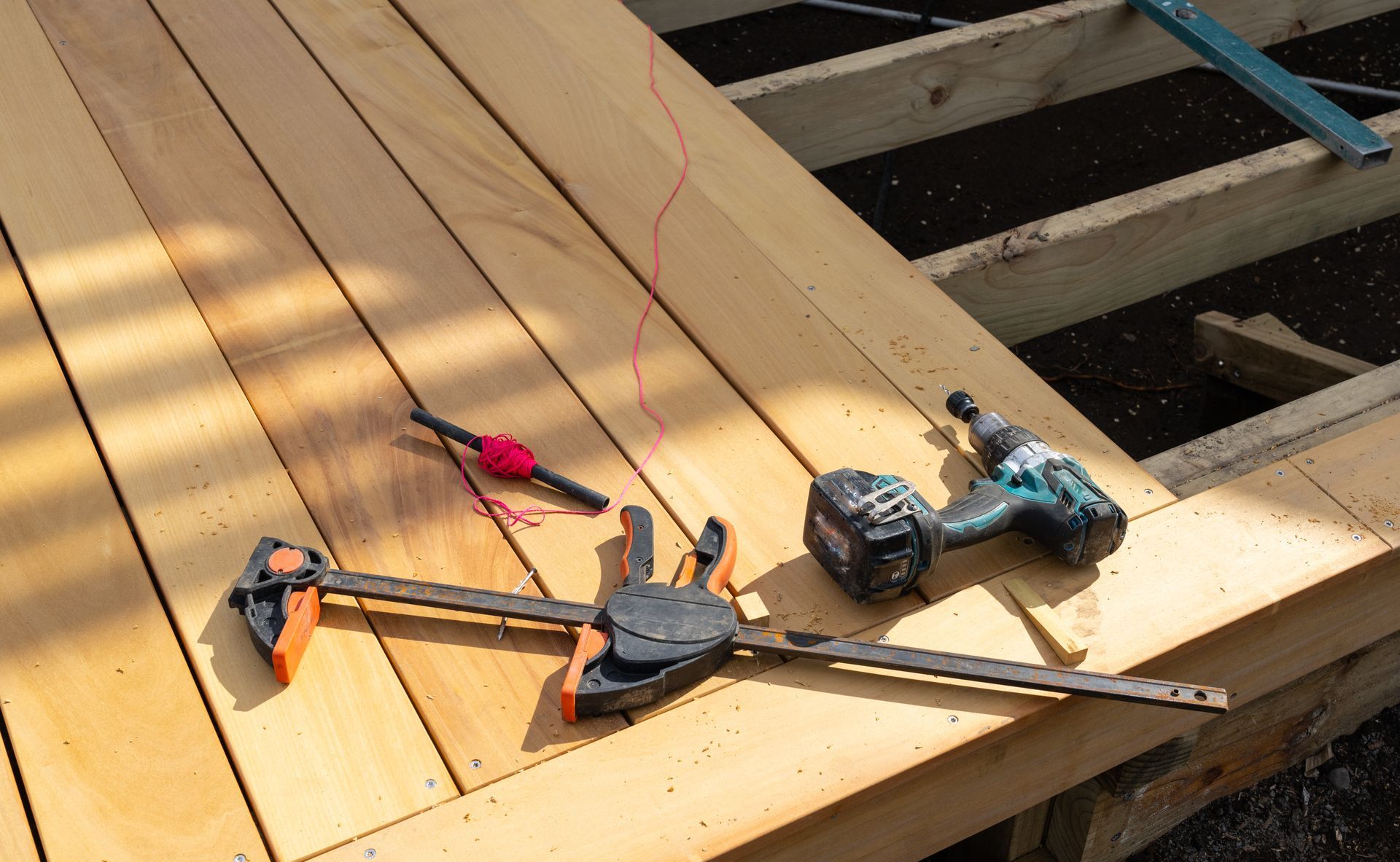 A drill and a bar clamp resting on freshly installed wooden deck boards during construction.