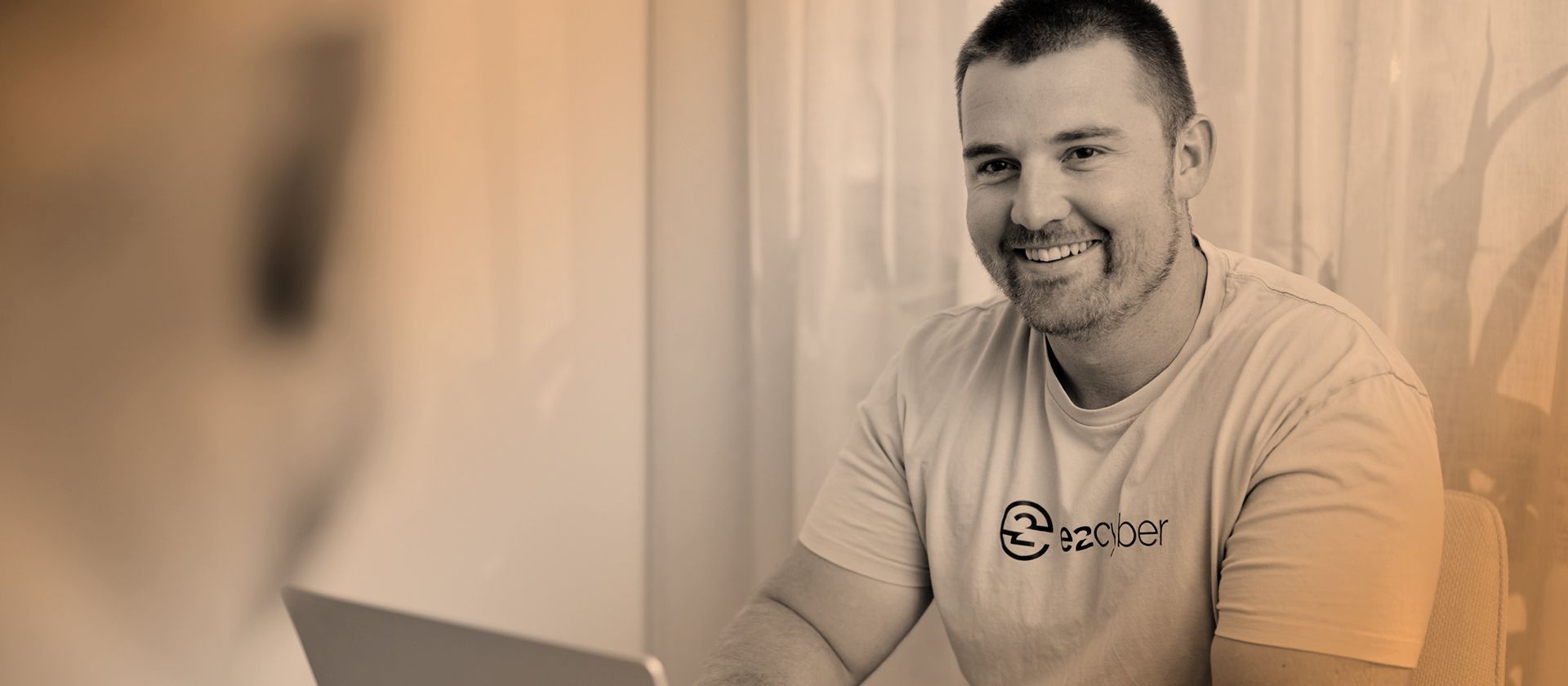 e2 cyber director Jacob Bywater sits in interview at desk with sepia filter and curtains