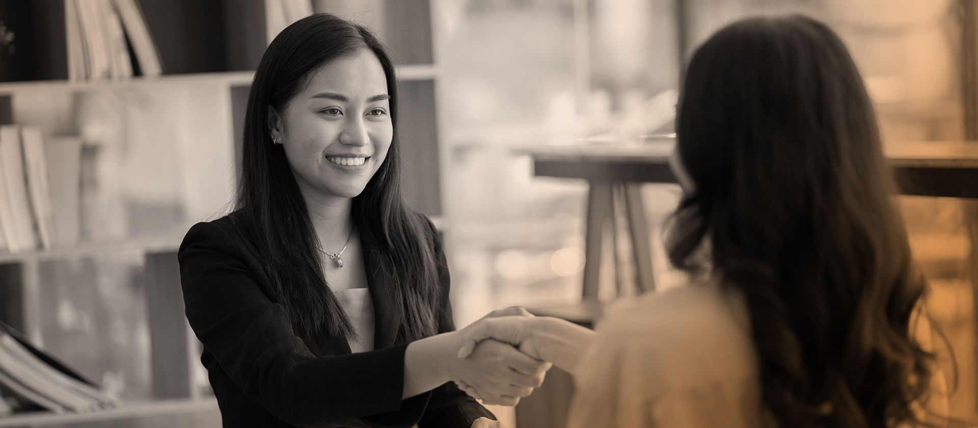 Two women are shaking hands during an interview in a black and white photo.