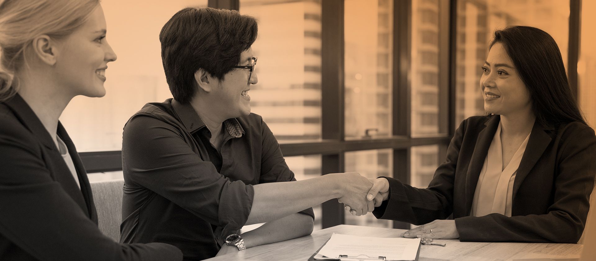 Three professional women at interview table shaking hands